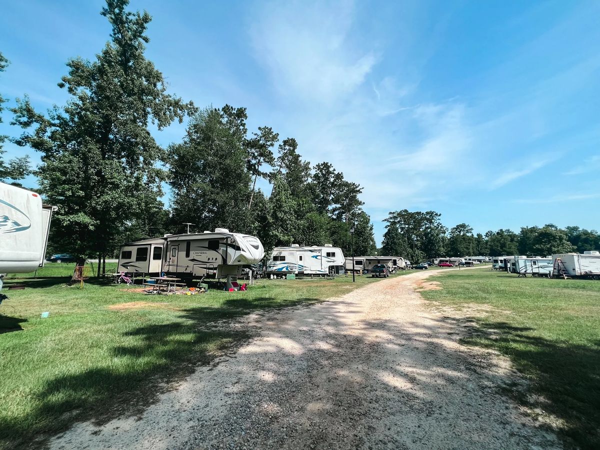 Fifth wheels and travel trailers on grassy RV sites under tall shade trees